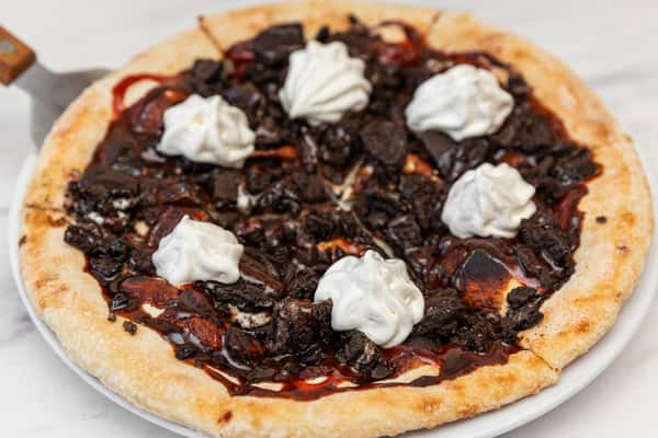 dessert pizza topped with chocolate sauce and dollops of whipped cream on a golden crust