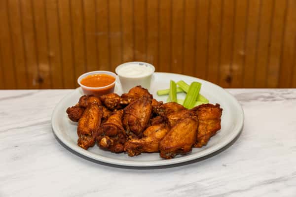 plate of crispy chicken wings with celery sticks and dipping sauces on the side