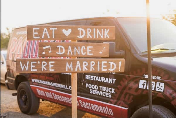 A wooden sign that says "Eat, Drink, Dance, We're Married" in front of a Paquita's Mexican Grill van