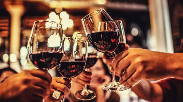 Hands clink glasses of red wine in a warm, dimly lit restaurant setting with festive bokeh lights