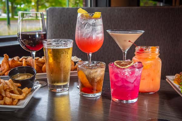 Assortment of colorful drinks including cocktails, beer, and wine on a table with appetizers in the background
