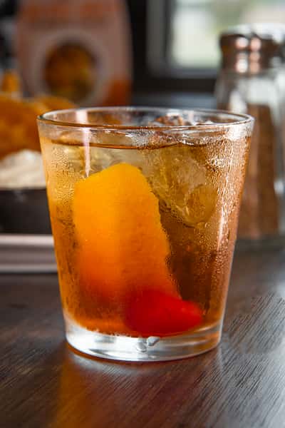 Close-up of an old fashioned cocktail with ice, an orange peel, and a cherry garnish in a short glass