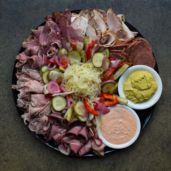 A platter of assorted deli meats including roast beef, turkey, and corned beef, accompanied by pickles, sauerkraut, onions, and two types of mustard sauces.