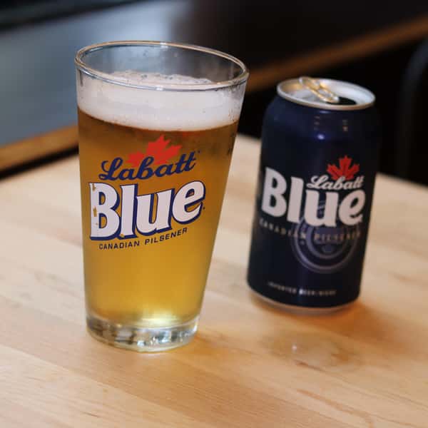 A glass of Labatt Blue Canadian Pilsner beer next to a can of Labatt Blue, both on a wooden table.