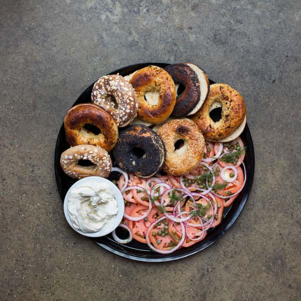 A platter of various toasted bagels, including sesame and plain, served with sliced tomatoes, onions, capers, fresh dill, and a side of cream cheese.