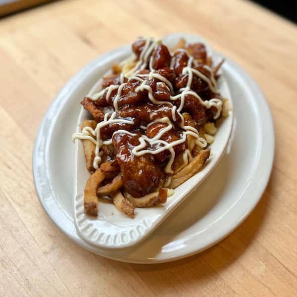 A plate of fries topped with a savory gravy, pulled meat, and drizzled with mayonnaise, resembling a twist on poutine.