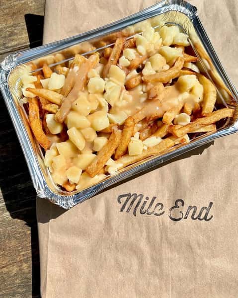 A tray of poutine with crispy fries topped with cheese curds and smothered in gravy, placed on a brown paper with the "Mile End" logo.