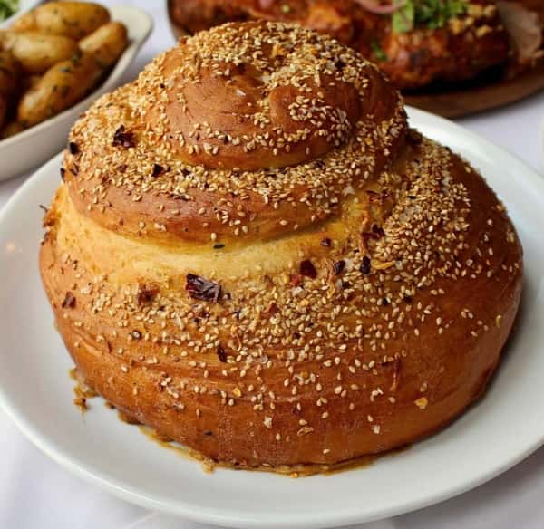 A round, freshly baked sesame-covered bread, slightly twisted in shape, with a golden-brown crust and sprinkled with sesame seeds.