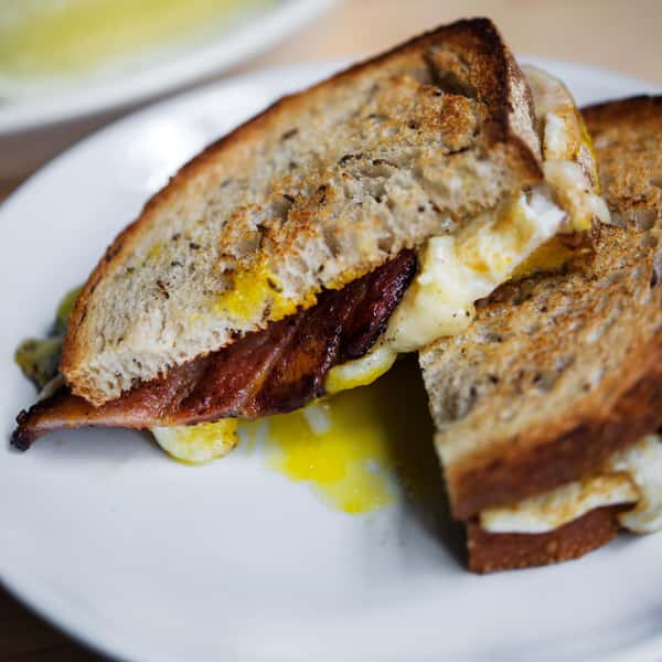 A toasted sandwich with crispy bacon, melted cheese, and a runny fried egg, served on whole grain bread.