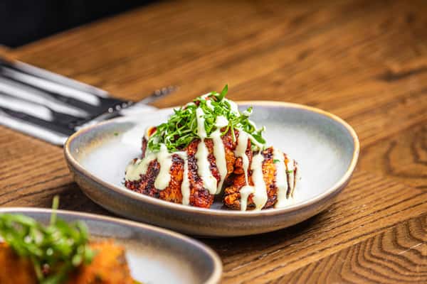 Chargrilled chicken wings drizzled with creamy white sauce, topped with fresh herbs and served in a rustic ceramic bowl.