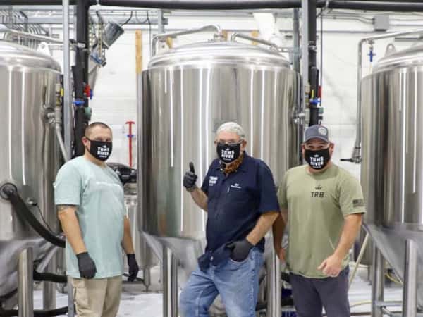 3 men standing in front of beer vat