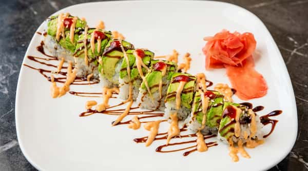 Avocado sushi rolls drizzled with spicy sauce and topped with fresh vegetables on a white plate