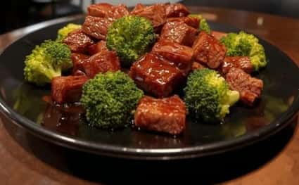 Crispy beef and broccoli stir-fry coated in a rich savory sauce and served on a black plate