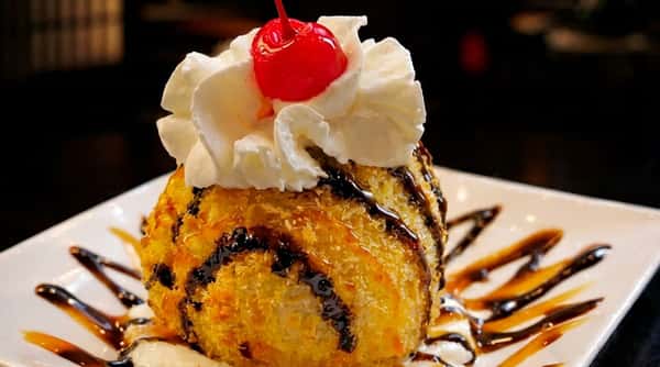 Dessert sushi roll topped with whipped cream, chocolate drizzle, and a maraschino cherry