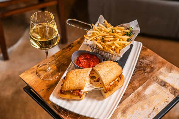 Crispy chicken parmesan sandwich with melted mozzarella and marinara on ciabatta, served with garlic fries and a glass of white wine — cozy Italian-American comfort food.