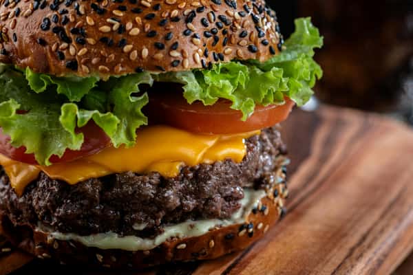 A sesame seed bun burger with beef, cheese, lettuce, and tomato sits on a wooden board at Spot Gourmet Burgers.