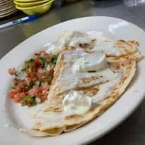 A plate of quesadillas with sour cream on top, accompanied by a side of fresh pico de gallo.
