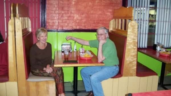 Two people laughing and sitting together in a booth at a brightly colored restaurant. The man is smiling and holding a snack while the woman laughs.