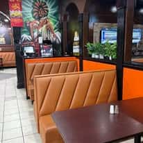 Restaurant booths with tan leather seating and dark wood tables, featuring vibrant wall art and orange panel accents.