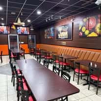 A view of the interior of a restaurant with seating arranged at tables along the walls, featuring brown and red chairs.
