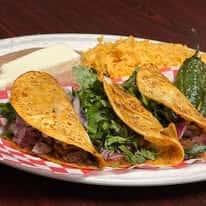Three tacos filled with beef, topped with onions and cilantro, accompanied by rice, beans, and a grilled poblano pepper.