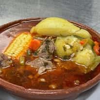 A traditional Mexican beef soup served in a clay pot, featuring pieces of beef, corn, potatoes, and vegetables in a flavorful broth.