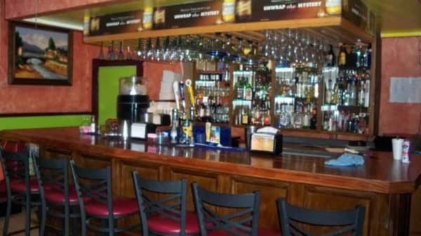 A view of a restaurant bar, featuring a variety of liquor bottles on the shelves, bar stools, and a clean, organized counter.