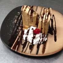 Churros drizzled with chocolate sauce and topped with whipped cream and a cherry on a beige plate.