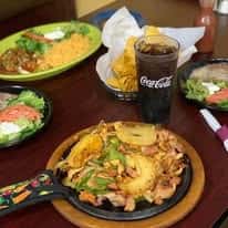 Table with sizzling chicken fajitas, Mexican rice, refried beans, tortilla chips, and a glass of Coca-Cola.