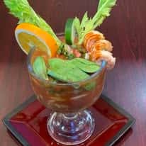 A seafood cocktail served in a glass, garnished with shrimp, orange, cucumber, and celery.