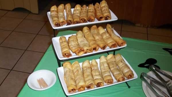 A three-tiered display of rolled-up appetizers, likely filled with a savory filling, alongside a small bowl of toothpicks and serving utensils.