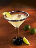 A glass of cocktail served with olives and a slice of lime