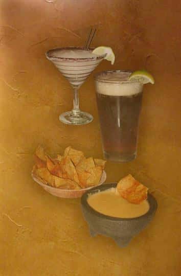 Two glasses of cocktails, a bowl of nachos and a bowl of dipping sauce