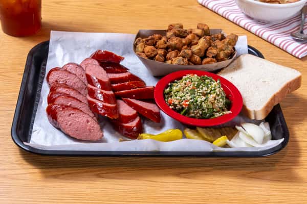 Smoked sausage and sliced barbecue meats served with fried okra, herb salad, white bread, and classic Southern sides.