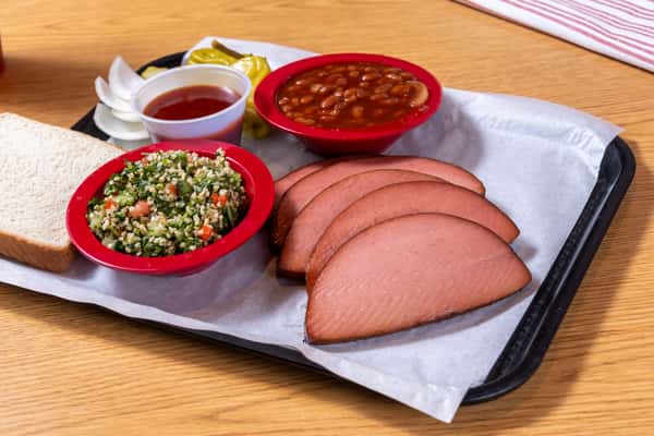 Sliced smoked ham served with baked beans, herb salad, white bread, pickles, and onions.