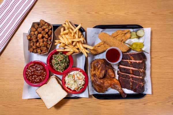 Family-style Southern barbecue feast with smoked ribs, brisket, fried catfish, roasted chicken, fries, baked beans, coleslaw, and classic sides.