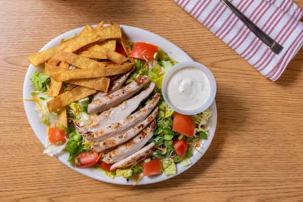 Grilled chicken salad with sliced chicken breast, fresh lettuce, tomatoes, shredded cheese, crunchy tortilla strips, and creamy dressing.
