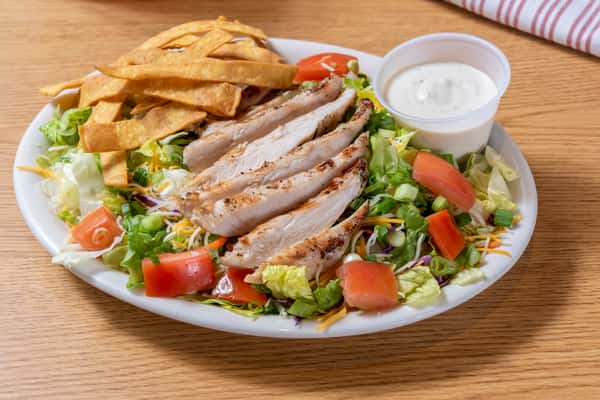 Grilled chicken salad with sliced chicken breast, fresh lettuce, tomatoes, shredded cheese, tortilla strips, and creamy dressing.