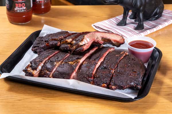 Smoked pork ribs with dark bark and BBQ sauce served on a lined tray at a Southern barbecue restaurant