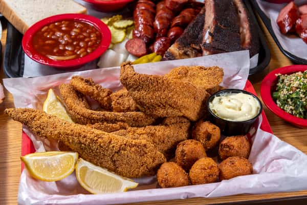 Golden fried catfish fillets with hushpuppies, lemon wedges, creamy dipping sauce, and Southern BBQ sides.