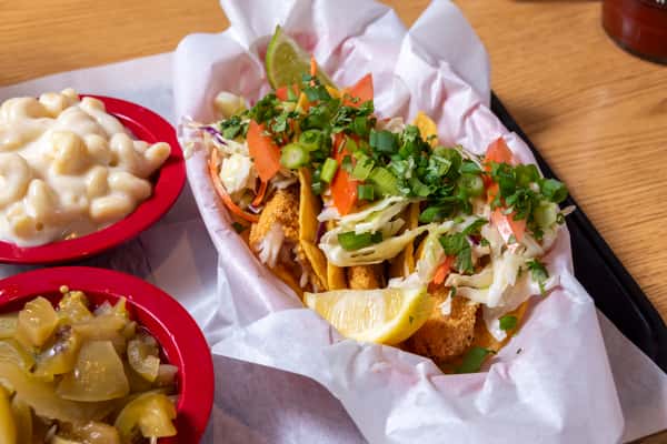Southern-style fried fish tacos topped with shredded cabbage, pico de gallo, fresh herbs, and lemon, served with classic sides.