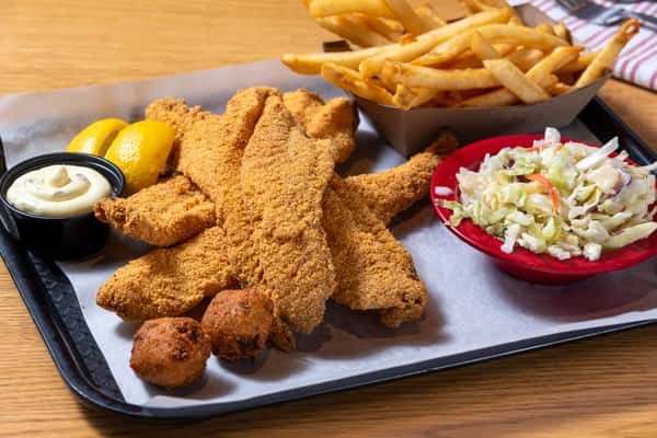 Fried catfish platter with golden breaded catfish fillets, French fries, coleslaw, hushpuppies, lemon wedges, and dipping sauce.