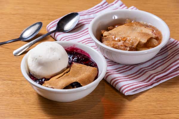Southern dessert bowls with warm fruit cobbler and vanilla ice cream alongside a slice of homestyle pie.