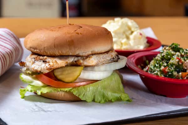 Grilled chicken sandwich with lettuce, tomato, onion, and pickles, served with potato salad and Southern sides.
