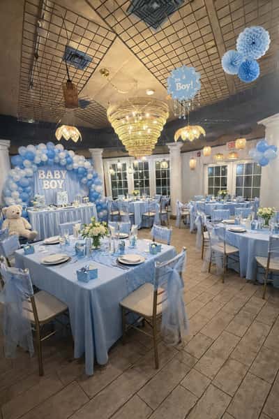 Elegant baby shower setup with blue "It's a Boy!" theme, round tables, balloon arch, and a large teddy bear near the dessert table.