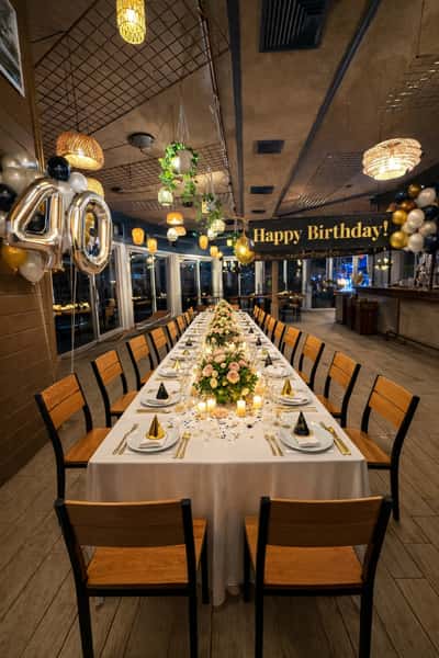 Elegant indoor 40th birthday dinner setup with long table, candles, floral centerpieces, gold accents, and "Happy Birthday!" banner.