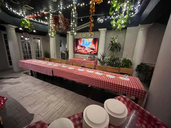 Long dining table with red-and-white checkered tablecloth, plates set, string lights overhead, greenery, and a fireplace backdrop.