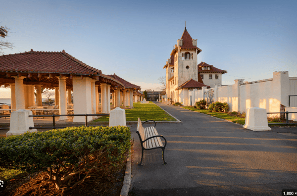 Elegant historic building with red-tiled roofs and open-air pavilion, surrounded by manicured lawns and sunset lighting.
