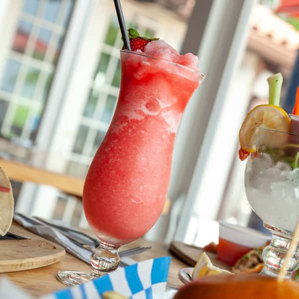Frozen strawberry daiquiri in a curved glass, garnished with a fresh strawberry and lime, served with a black straw.