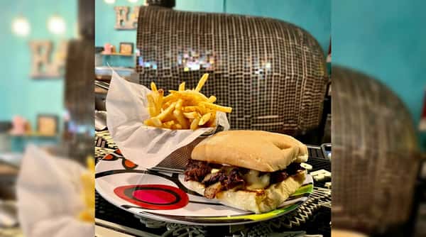 Philly cheesesteak sandwich with melted cheese and fries in a metal basket on an abstract plate.
